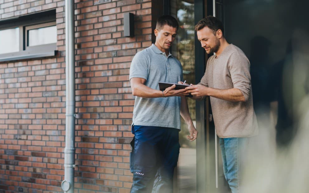 Cliente finale che firma l'offerta di finanziamento - entrambi in piedi davanti alla porta principale